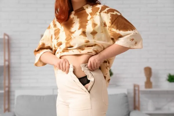 Image of woman trying to do her trousers up after pregnancy weight gain Binton