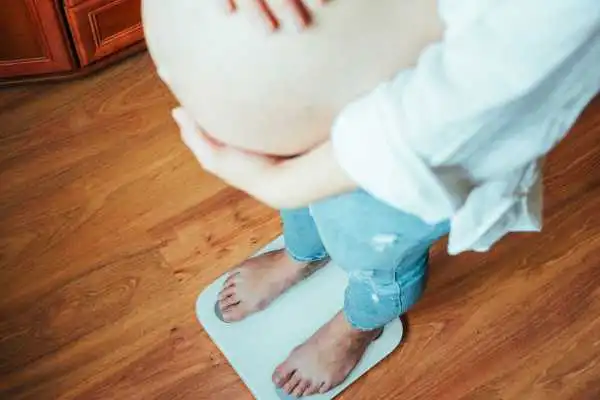 Image of woman weighing herself and experiencing weight gain through pregnancy Binton